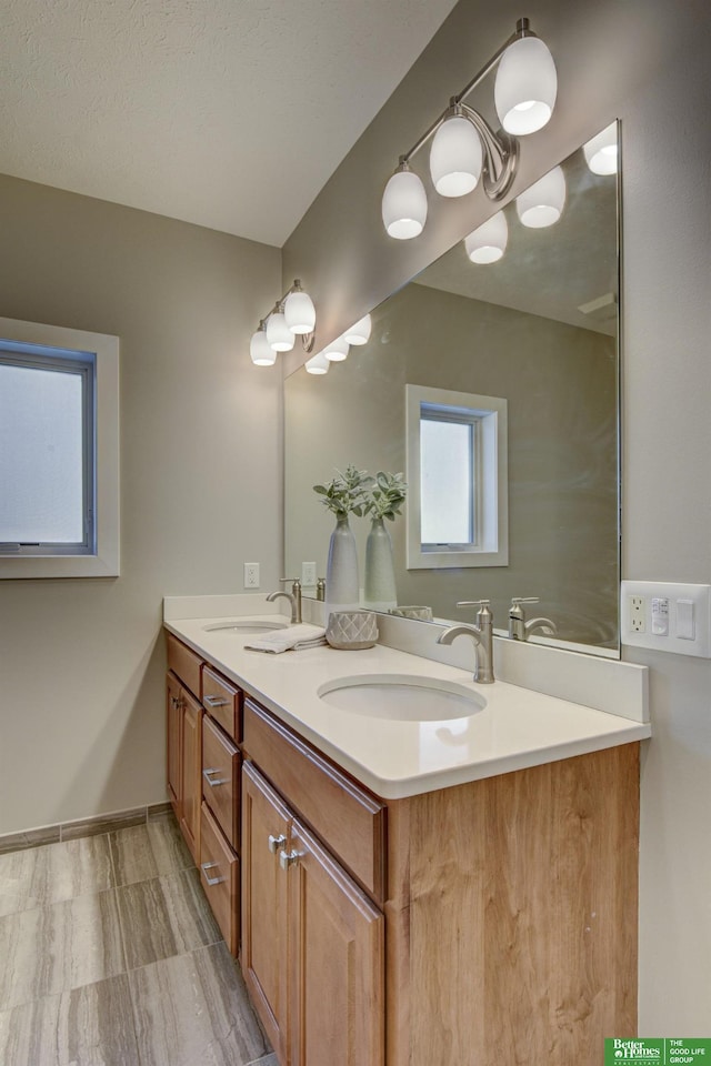 bathroom with a textured ceiling, double vanity, baseboards, and a sink