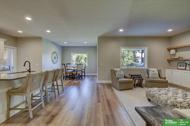 living room featuring recessed lighting, baseboards, a textured ceiling, and light wood-style flooring