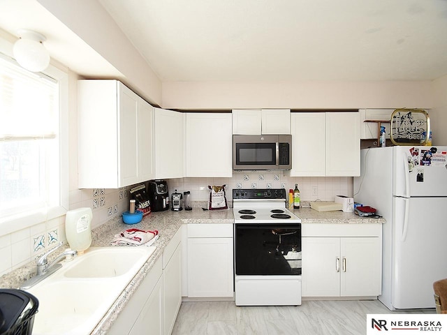 kitchen featuring stainless steel microwave, range with electric cooktop, white cabinets, and freestanding refrigerator