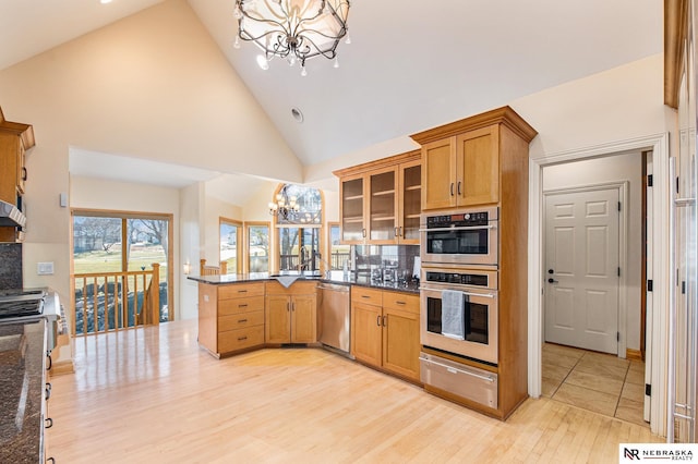 kitchen featuring a warming drawer, a notable chandelier, stainless steel appliances, a peninsula, and glass insert cabinets