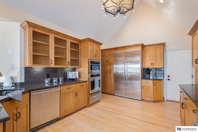 kitchen featuring light wood finished floors, glass insert cabinets, dark stone countertops, appliances with stainless steel finishes, and a sink