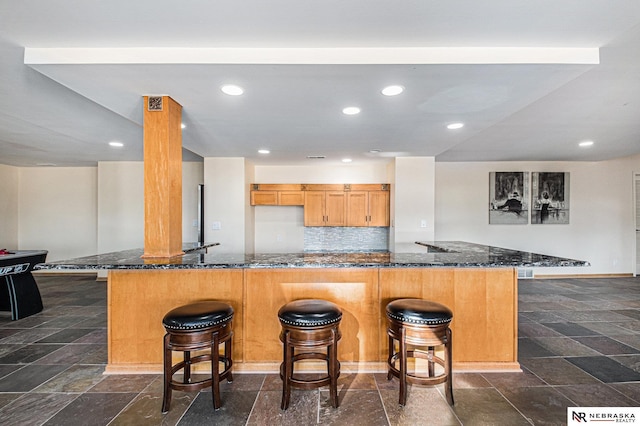 kitchen with stone tile floors, decorative backsplash, a breakfast bar, and dark stone counters