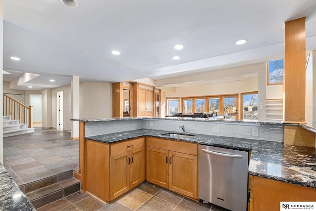 kitchen with open floor plan, dark stone counters, stone tile floors, stainless steel dishwasher, and a sink