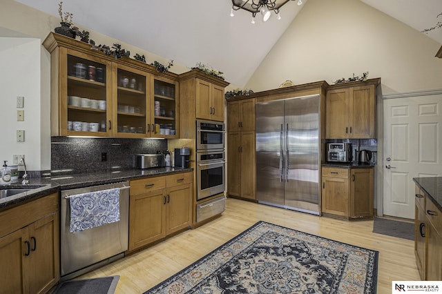 kitchen with dark stone counters, stainless steel appliances, decorative backsplash, glass insert cabinets, and light wood-style floors