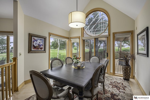 dining area featuring baseboards, light wood finished floors, and high vaulted ceiling