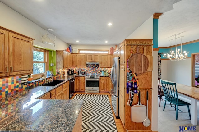 kitchen featuring a sink, under cabinet range hood, tasteful backsplash, dark stone counters, and appliances with stainless steel finishes