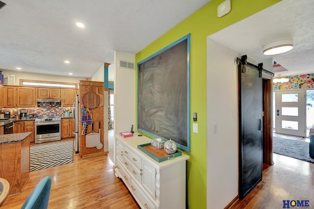 kitchen featuring visible vents, stainless steel appliances, decorative backsplash, under cabinet range hood, and a barn door