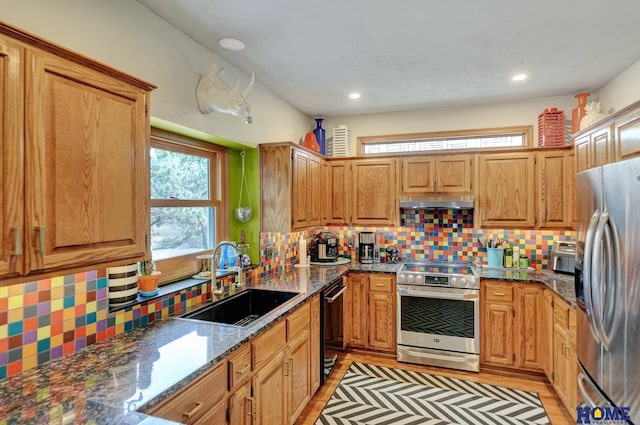 kitchen featuring a sink, under cabinet range hood, dark stone counters, appliances with stainless steel finishes, and decorative backsplash