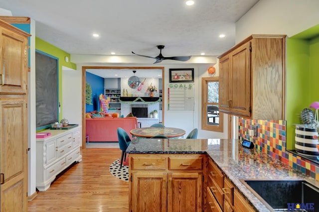 kitchen with a peninsula, recessed lighting, a fireplace, light wood-type flooring, and backsplash