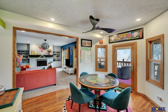 dining room with a textured ceiling, recessed lighting, light wood-style floors, a fireplace, and ceiling fan