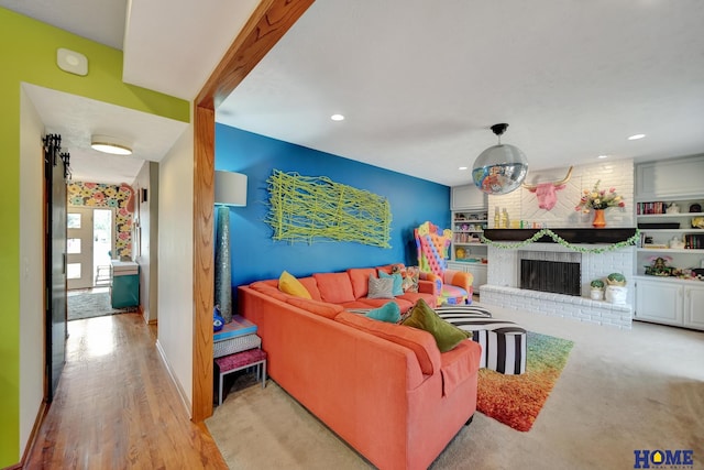 living area with recessed lighting, baseboards, a brick fireplace, and wood finished floors