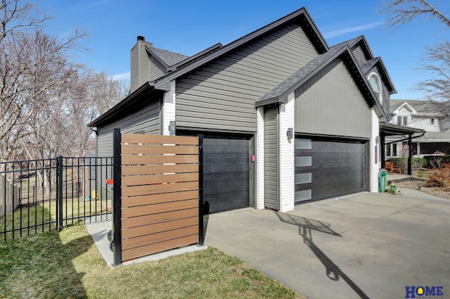 view of side of property featuring an attached garage, fence, driveway, and a chimney