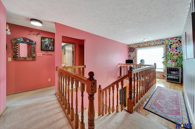 hallway featuring carpet flooring, an upstairs landing, baseboards, and a textured ceiling