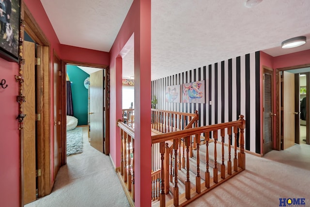 hall featuring wallpapered walls, an upstairs landing, carpet floors, and a textured ceiling