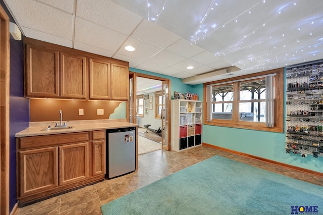 kitchen featuring brown cabinetry, a sink, light countertops, a paneled ceiling, and fridge