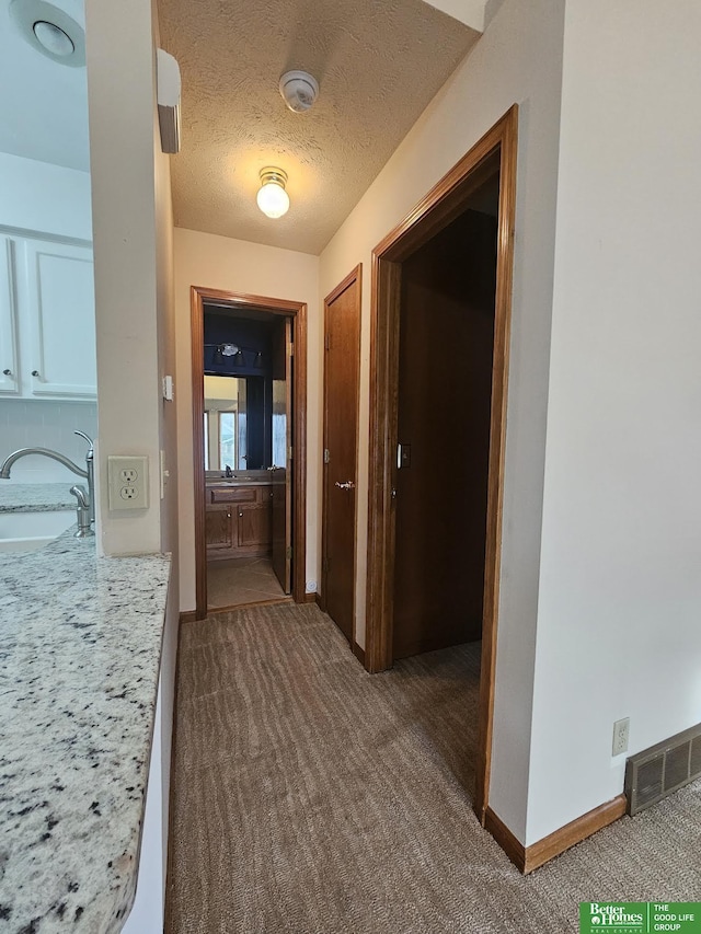 hallway featuring visible vents, baseboards, carpet, a textured ceiling, and a sink