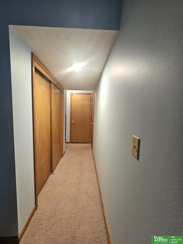 hallway featuring light carpet, a textured ceiling, and baseboards