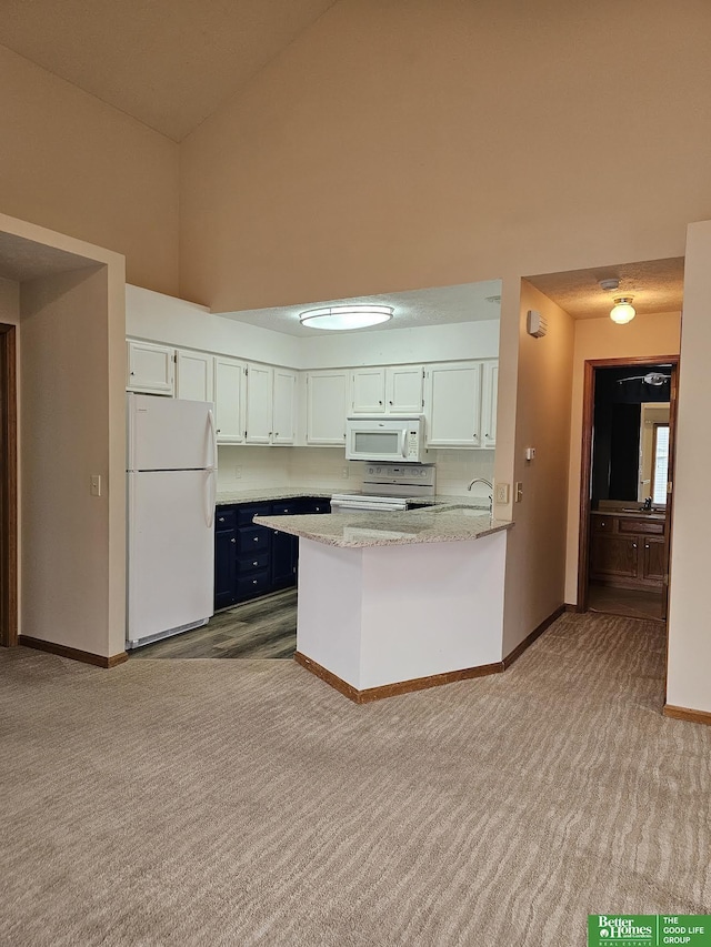 kitchen with white appliances, carpet, baseboards, a peninsula, and white cabinets