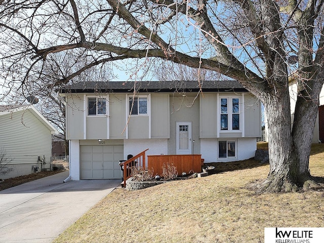 bi-level home with a garage, brick siding, and concrete driveway