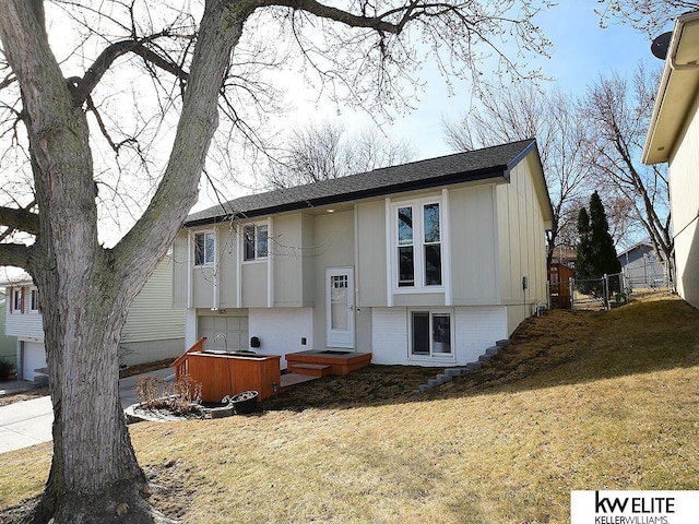 split foyer home with brick siding, a shingled roof, fence, a front yard, and an attached garage