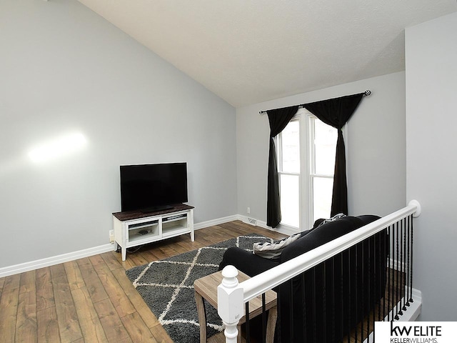 living room featuring hardwood / wood-style floors, lofted ceiling, and baseboards