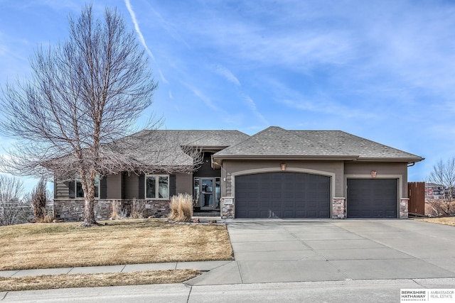 view of front of home featuring stone siding, roof with shingles, concrete driveway, a front yard, and a garage