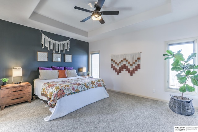 carpeted bedroom with a raised ceiling, a ceiling fan, and baseboards