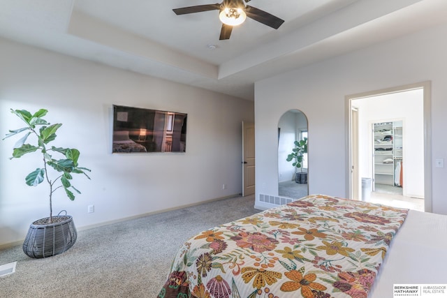 carpeted bedroom featuring visible vents, a ceiling fan, a tray ceiling, arched walkways, and baseboards