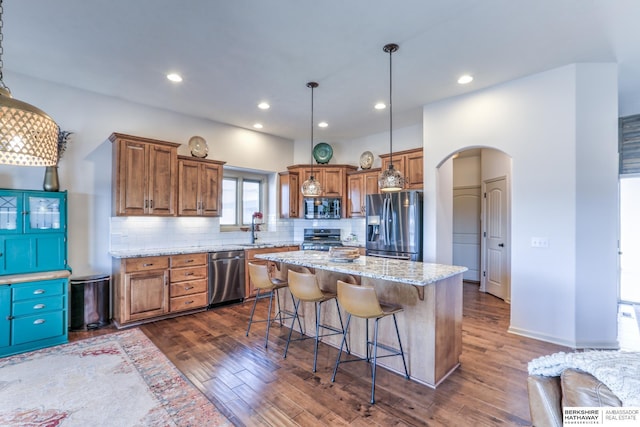 kitchen with a sink, stainless steel appliances, arched walkways, and brown cabinetry