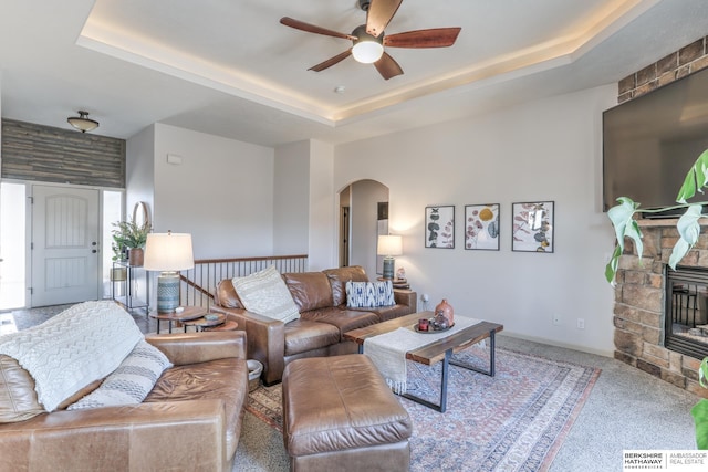 carpeted living area with a raised ceiling, a fireplace, and arched walkways