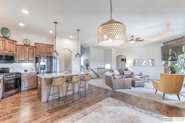 kitchen with brown cabinetry, a kitchen breakfast bar, arched walkways, stainless steel appliances, and wood-type flooring