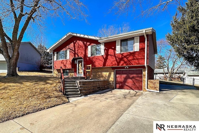 raised ranch featuring brick siding, concrete driveway, a garage, and fence