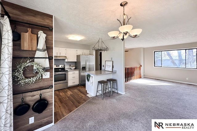 kitchen with dark carpet, a breakfast bar, a peninsula, a textured ceiling, and stainless steel appliances