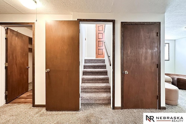 staircase featuring carpet flooring, a textured ceiling, and baseboards