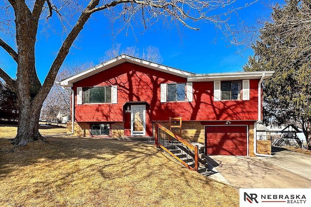 raised ranch with a garage, brick siding, concrete driveway, and a front yard