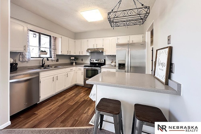 kitchen featuring dark wood-style flooring, appliances with stainless steel finishes, white cabinetry, and a sink