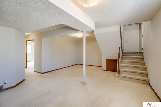 finished below grade area with visible vents, a textured ceiling, stairway, carpet floors, and baseboards