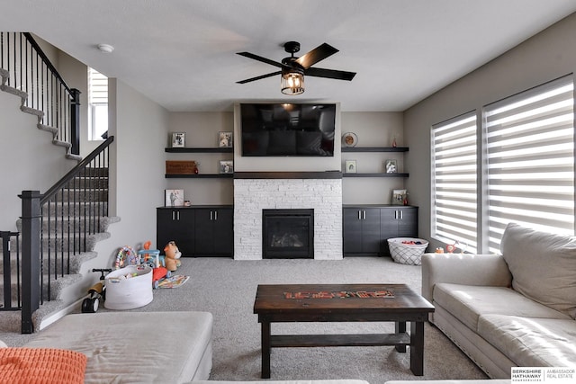 living area with a stone fireplace, stairway, a ceiling fan, and carpet floors