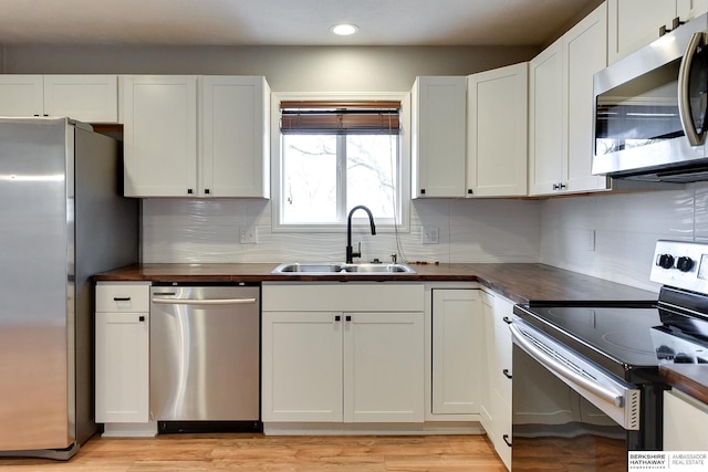 kitchen featuring light wood finished floors, backsplash, white cabinets, stainless steel appliances, and a sink