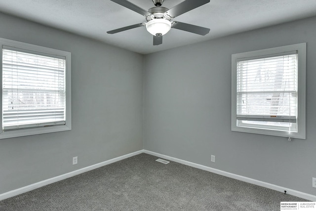 spare room featuring a wealth of natural light, visible vents, baseboards, and dark carpet