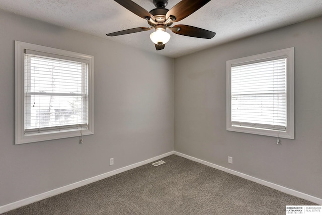 spare room featuring visible vents, a textured ceiling, a healthy amount of sunlight, and dark carpet