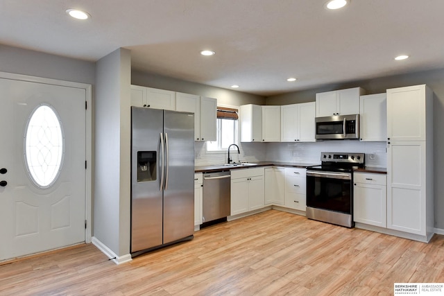 kitchen featuring a sink, stainless steel appliances, dark countertops, light wood-type flooring, and backsplash