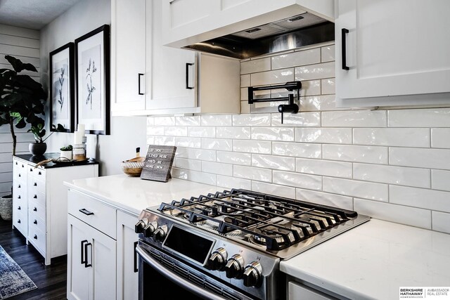 kitchen featuring tasteful backsplash, gas range, white cabinetry, and wall chimney range hood