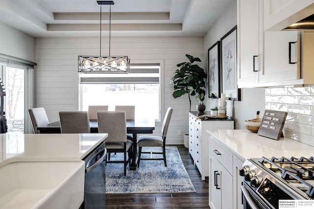 dining area with a chandelier, a raised ceiling, wooden walls, and dark wood-style floors