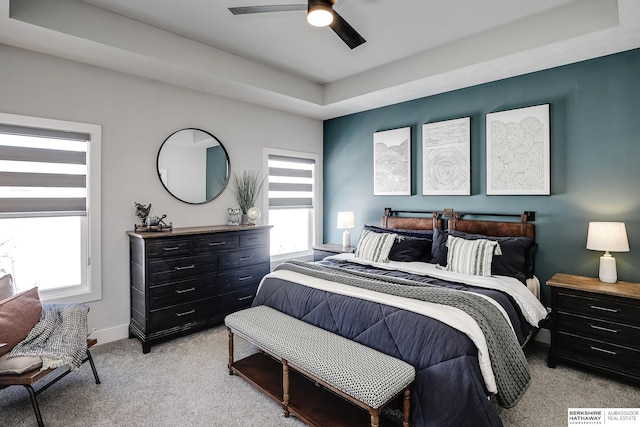 bedroom featuring a tray ceiling, baseboards, light colored carpet, and ceiling fan