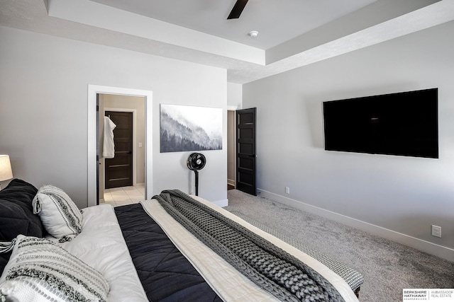 bedroom with baseboards, light colored carpet, a raised ceiling, and ensuite bath