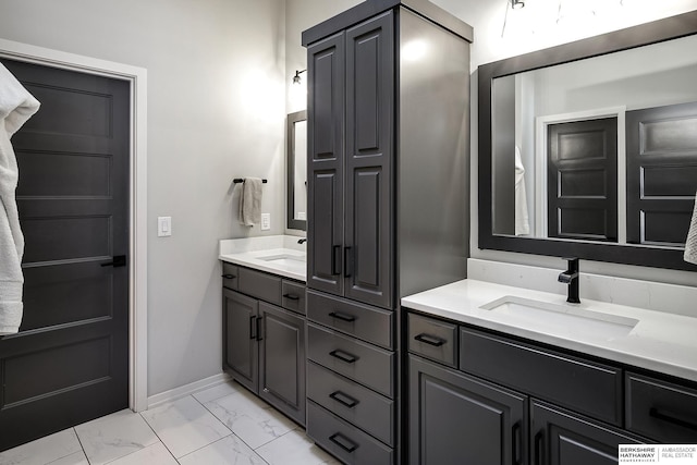 full bath featuring marble finish floor, two vanities, baseboards, and a sink