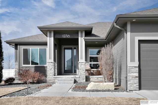 view of exterior entry with stone siding and roof with shingles