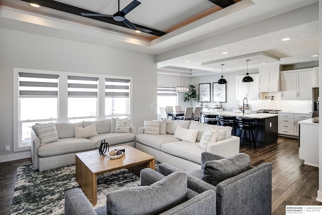 living room featuring a tray ceiling, dark wood-style floors, recessed lighting, baseboards, and ceiling fan