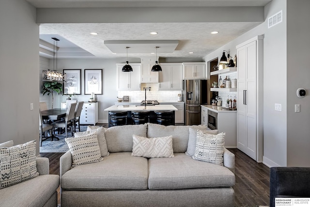 living room with visible vents, a tray ceiling, recessed lighting, baseboards, and dark wood-style flooring